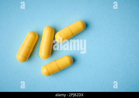 Gelbe Gelatinekapseln Pillen, orales Medikament gefüllt mit Pulver oder flüssige Form auf blauem Hintergrund, direkt von oben mit Copy Space genommen Stockfoto