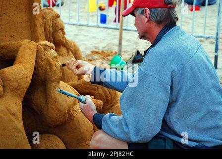 Ein Bildhauer schneidet die Details einer Sandburg heraus Stockfoto