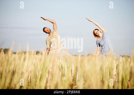 In perfekter Harmonie. Ein reifes Paar, das ein Yoga-Workout auf einem Feld genießt. Stockfoto