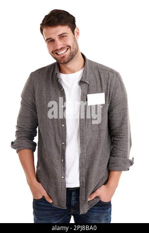 Dieses Namensschild kannst du ausfüllen. Studio-Porträt eines lächelnden jungen Mannes mit einem leeren Namensschild, der mit den Händen in den Taschen steht. Stockfoto