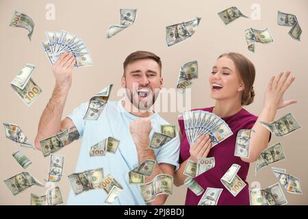 Glückliche junge Leute mit Geld und fallenden amerikanischen Dollars auf beigefarbenem Hintergrund Stockfoto