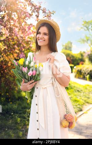 Wunderschöne junge Frau mit einem Strauß aus Tulpen und Äpfeln im Park an sonnigen Tagen Stockfoto