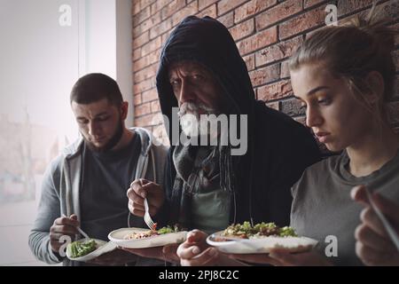 Arme Leute mit Essenstellern an der Wand drinnen Stockfoto