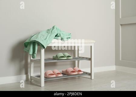 Elegante Aufbewahrungsbank mit verschiedenen Paar Gummipantoffeln an der weißen Wand im Flur Stockfoto