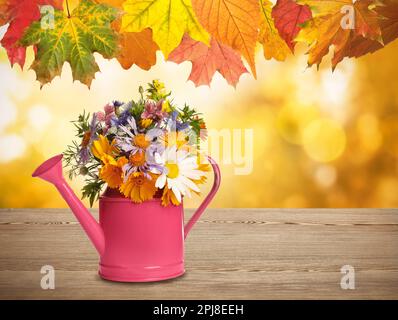 Herbstblätter über einem Blumenstrauß in der Gießkanne auf dem Holztisch, Platz für Text Stockfoto