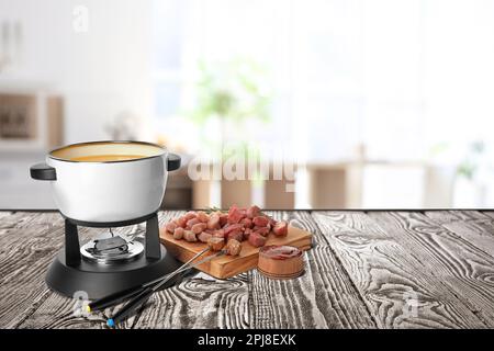 Zusammensetzung mit Fondue-Topf und Fleisch auf Holztisch in der Küche. Platz für Text Stockfoto