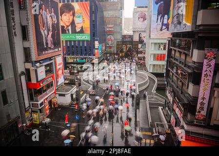 OSAKA, JAPAN - 16. AUGUST 2015: Fußgänger laufen an regnerischen Tagen unter Plakaten im Dotonbori-Viertel. Stockfoto