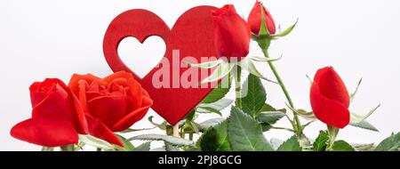 Detail mit roten Rosen in Blumenform mit Holzherz vor weißem Hintergrund. Konzept der Liebe und Valentinstag. Banner-Kopfzeilenbild. Stockfoto