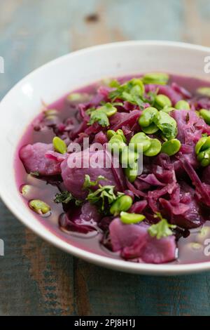 Schüssel mit einer hausgemachten violetten Kohlsuppe mit violetten Kartoffeln und Fava-Bohnen. Stockfoto