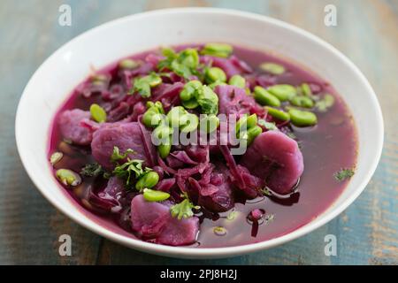 Schüssel mit einer hausgemachten violetten Kohlsuppe mit violetten Kartoffeln und Fava-Bohnen. Stockfoto