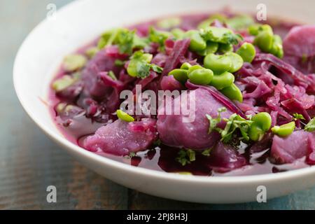 Schüssel mit einer hausgemachten violetten Kohlsuppe mit violetten Kartoffeln und Fava-Bohnen. Stockfoto