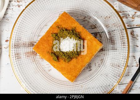 Revani-Dessert auf Holzhintergrund. Traditionelles Ramadan-Dessert. Revani Nachtisch mit Pistazien und Kokosnuss. Draufsicht Stockfoto
