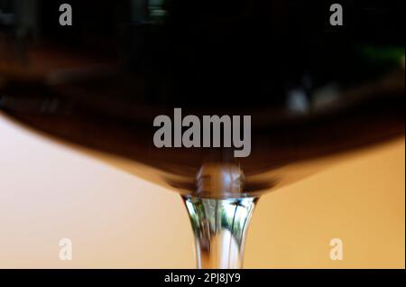 Der Stiel eines Weinglases im Detail, das Glas ist voller Rotwein. Die Unterseite des Glases scheint sich stärker zu verformen als sie. Stockfoto