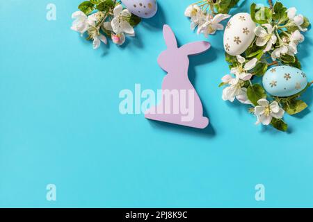 Ostergemisch mit bunten Eiern, Holzhasen und Frühlingsblumen auf blauem Hintergrund. Frühlingskonzept, Blumenzusammensetzung. Grußkarte. Anzeigen Stockfoto