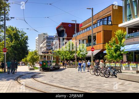 31. Dezember 2022: Christchurch, Neuseeland - Leute genießen einen Sommertag im Terrace, einem neuen Flussufer-Bauwerk. Mit einer nahenden Straßenbahn. Stockfoto