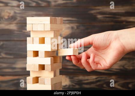 Eine Geschäftsfrau sucht sich das letzte Stück des Holzpuzzels aus und legt es hin. Abstraktes Geschäftskonzept der letzten wichtigen Lösung in der Strategie. Stockfoto