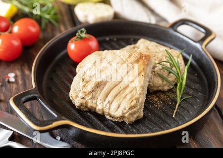Essen im Restaurant. Meeresfrüchte. Rustikaler Stil. Gekochtes saftiges Thunfischsteak mit Gewürzen, Tomaten und Rosmarin auf einer Steinplatte. Stockfoto