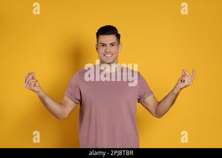 Hübscher Mann, der Finger auf gelbem Hintergrund schnappte Stockfoto