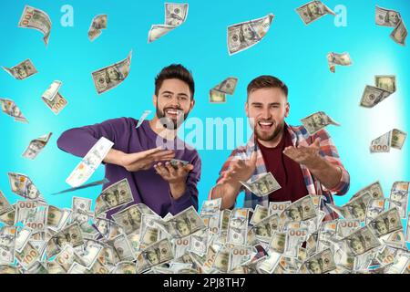 Glückliche junge Männer mit Geld und fallenden amerikanischen Dollars auf türkisfarbenem Hintergrund Stockfoto