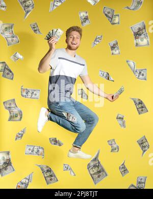 Glücklicher junger Mann mit Geld und fallenden amerikanischen Dollars auf gelbem Hintergrund Stockfoto