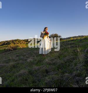 Junge Frau in Cottage-Kleid und knöpftem Oberteil beim Spaziergang in den Palo Alto Hills Aussicht | Blumenstrauß | Blumenbügel Stockfoto