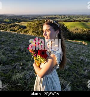 Junge Frau in Cottage-Kleid und knöpftem Oberteil beim Spaziergang in den Palo Alto Hills Aussicht | Blumenstrauß | Blumenbügel Stockfoto