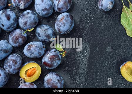 Pflaumen in Wassertropfen auf dem Hintergrund eines schwarzen Steinbretts. Draufsicht mit Kopierbereich. Schöne, reife Pflaumen, die im Herbst Früchte ernten Stockfoto