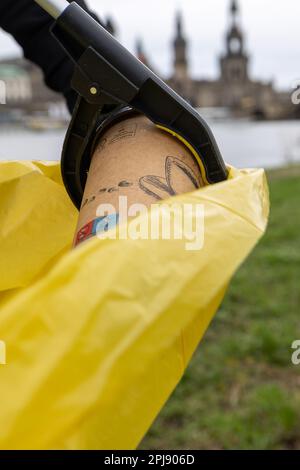 Dresden, Deutschland. 01. April 2023. Eine Kaffeetasse wird während des Reinigungstages der Elbe Meadows in der Stadt Dresden in eine gelbe Tüte mit einem Greifer gegeben. Das Einsatzgebiet erstreckt sich auf beiden Seiten der Elbe von Cossebaude bis Pillnitz und ist insgesamt 30 km lang. Kredit: Daniel Schäfer/dpa/Alamy Live News Stockfoto