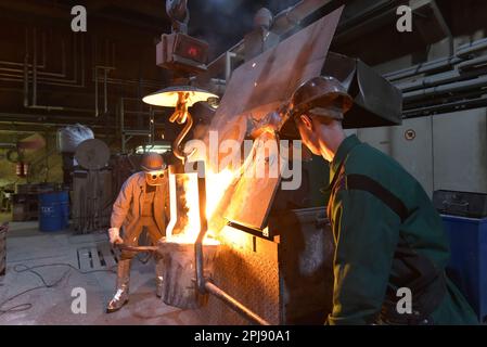 Arbeitnehmer in einer Gießerei gießen ein Werkstück aus Metall - Sicherheit bei der Arbeit und Teamarbeit Stockfoto