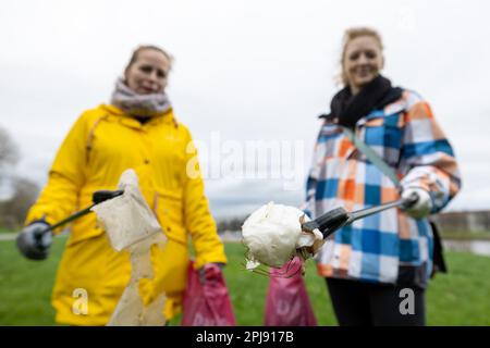 Dresden, Deutschland. 01. April 2023. Zwei Frauen strecken ihre Hände mit Müll in die Kamera, anlässlich der Reinigung der Elbwiese in der Stadt Dresden. Das Einsatzgebiet der erstreckt sich auf beiden Seiten der Elbe von Cossebaude bis Pillnitz und ist insgesamt 30 km lang. Kredit: Daniel Schäfer/dpa/Alamy Live News Stockfoto