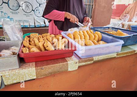 Eine Nebenansicht einer nicht identifizierten Frau, die indonesisches Street Food verkauft. Eine Art takjil, die perfekt frittiert ist. Ramadan 2023 Stockfoto