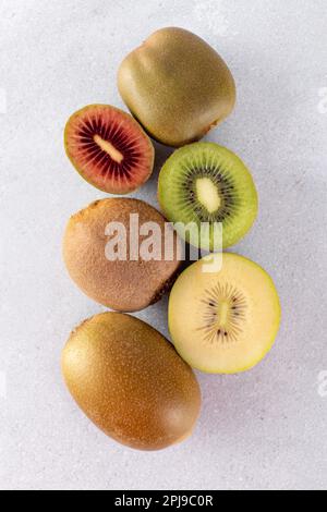 Verschiedene Kiwis liegen auf einem Stapel auf dem Tisch. Hälften roter, gelber und grüner Kiwi. Stockfoto
