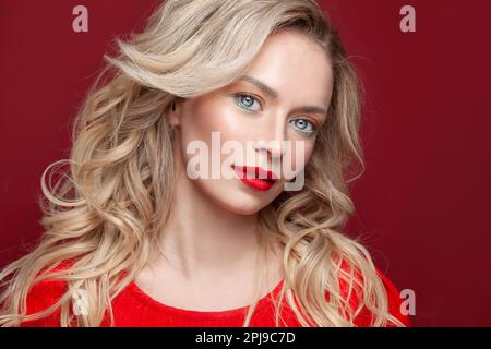 Perfekte Frau mit blondem Haar und Make-up auf rotem Hintergrund Stockfoto