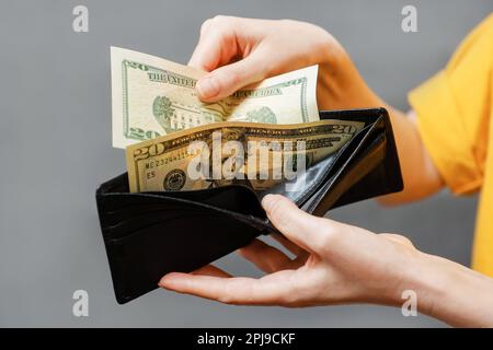 Ersparnisse. Frauenhände nehmen Dollarscheine aus einer schwarzen Lederbörse. Nahaufnahme. Das Konzept des Einkaufs und der Bezahlung. Stockfoto