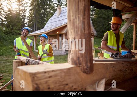 Bauarbeiter haben gute Laune, wenn sie an einem wunderschönen Tag auf der Baustelle des Cottage im Wald arbeiten. Arbeiter, Bauarbeiter, Natur Stockfoto