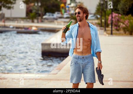 Ein lächelnder Mann im Urlaub genießt einen sonnigen Tag und trinkt ein Bier Stockfoto