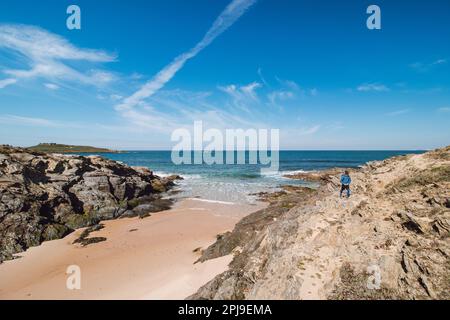 Backpacker wandern entlang eines Felsens und über einen Sandstrand auf dem markierten Fisherman Trail an der Atlantikküste in der Nähe von Porto Covo, Portugal. Rota Vicentina. Stockfoto