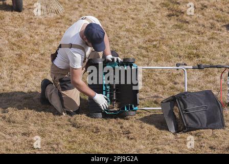 Mann Gärtner Reinigungsmaschine scarifier von alten trockenen Gras auf dem Rasen Stockfoto