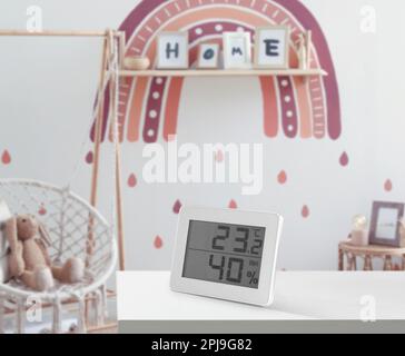 Digitales Hygrometer mit Thermometer auf weißem Tisch im Kinderzimmer. Optimale Luftfeuchtigkeit für Kinder Stockfoto