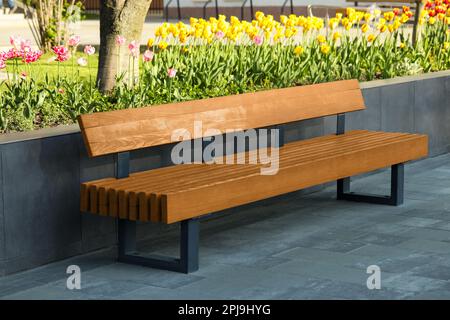 Holzbank neben dem Blumenbeet im Freien an sonnigen Morgen Stockfoto