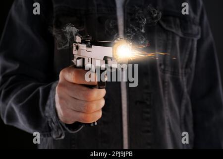 Ein Mann, der auf schwarzem Hintergrund mit einer Waffe schießt, Nahaufnahme Stockfoto