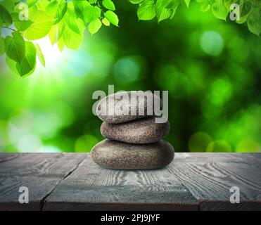 Gestapelte Steine auf einem Holztisch unter grünen Blättern vor verschwommenem Hintergrund. Zen-Konzept Stockfoto