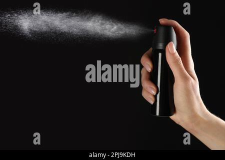 Frau, die Pfefferspray auf schwarzem Hintergrund benutzt, Nahaufnahme Stockfoto