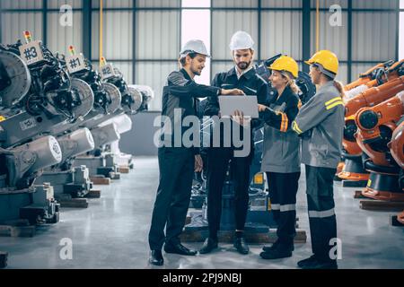 Die Gruppe der Ingenieure steht im Gespräch. Teamarbeit in der Branche – Mitarbeitergespräch. Zusammenkunft des Montagewerks für Roboterarme mit Laptop CO Stockfoto