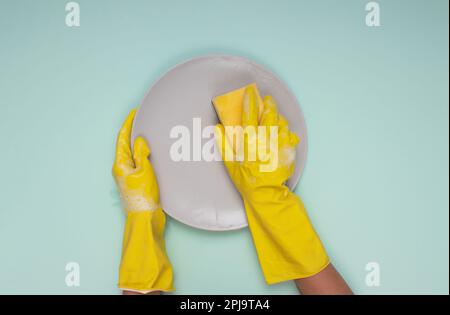 Frau in gelben Reinigungshandschuhen auf einer Reinigungsplatte mit hellem Hintergrund und Reinigungsschwamm Stockfoto