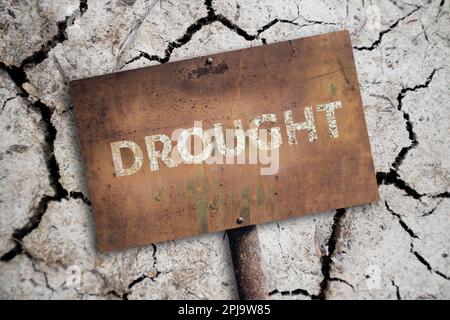 Ein rostiges Schild mit der Inschrift DÜRRE auf dem Hintergrund einer Wüste mit gerissenem Boden. Hochwertige Fotos Stockfoto