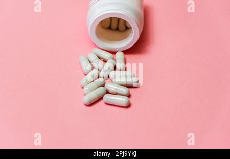 Pillen aus der weißen Flasche auf rosa Hintergrund. Modell für Sonderangebote wie Werbung oder andere Ideen. Medizin, Apotheke und Gesundheitswesen conce Stockfoto