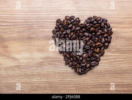 Konzept von Liebe oder Kaffee lieben. Herzform aus Kaffeebohnen auf einem Holzbrett. Stockfoto
