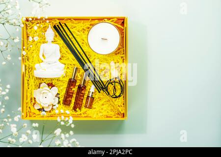 Urlaubskomposition mit Erholungsset für Meditation, Yoga und Entspannung. Gelbe Geschenkbox mit buddha-Statue, Aromastifte, natürliche Öle, Kerze und Stockfoto