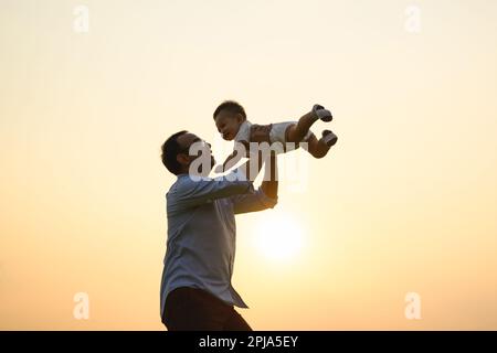 Glücklicher Vater hält das Neugeborene und spielt mit Blick auf den Sonnenuntergang Stockfoto